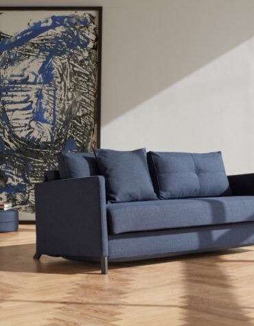 blaues Klappsofa in Wohnzimmer mit Parkettboden und Gemälde im Hintergrund